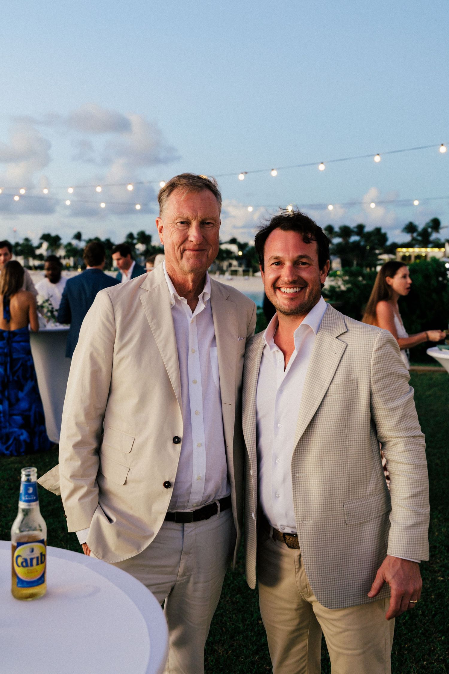 Three men in light colored suits pose together at outdoor evening event.