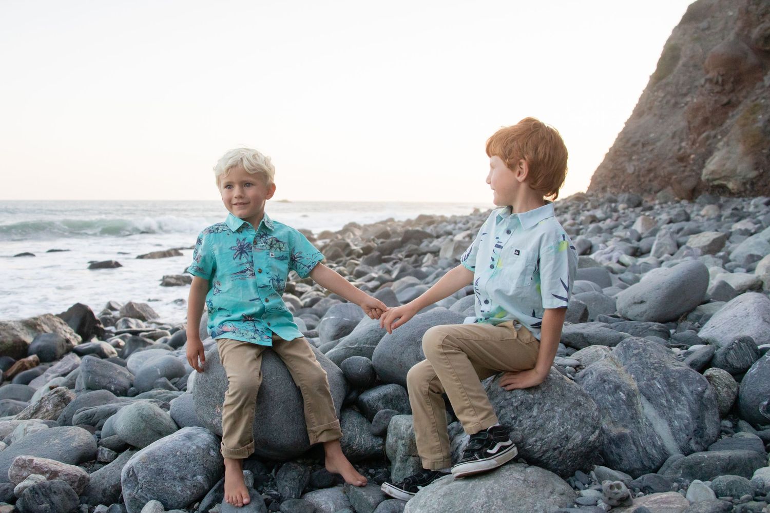 Children perched on black rocks along a scenic beach coastline.