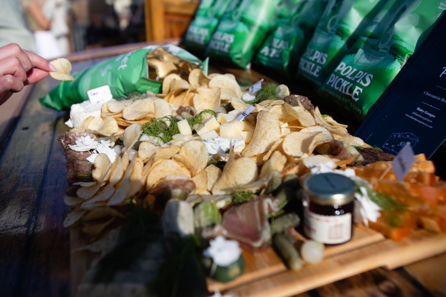 A platter of crisps topped with fresh toppings displayed near green bags of Bob's Pickle products at a food market.