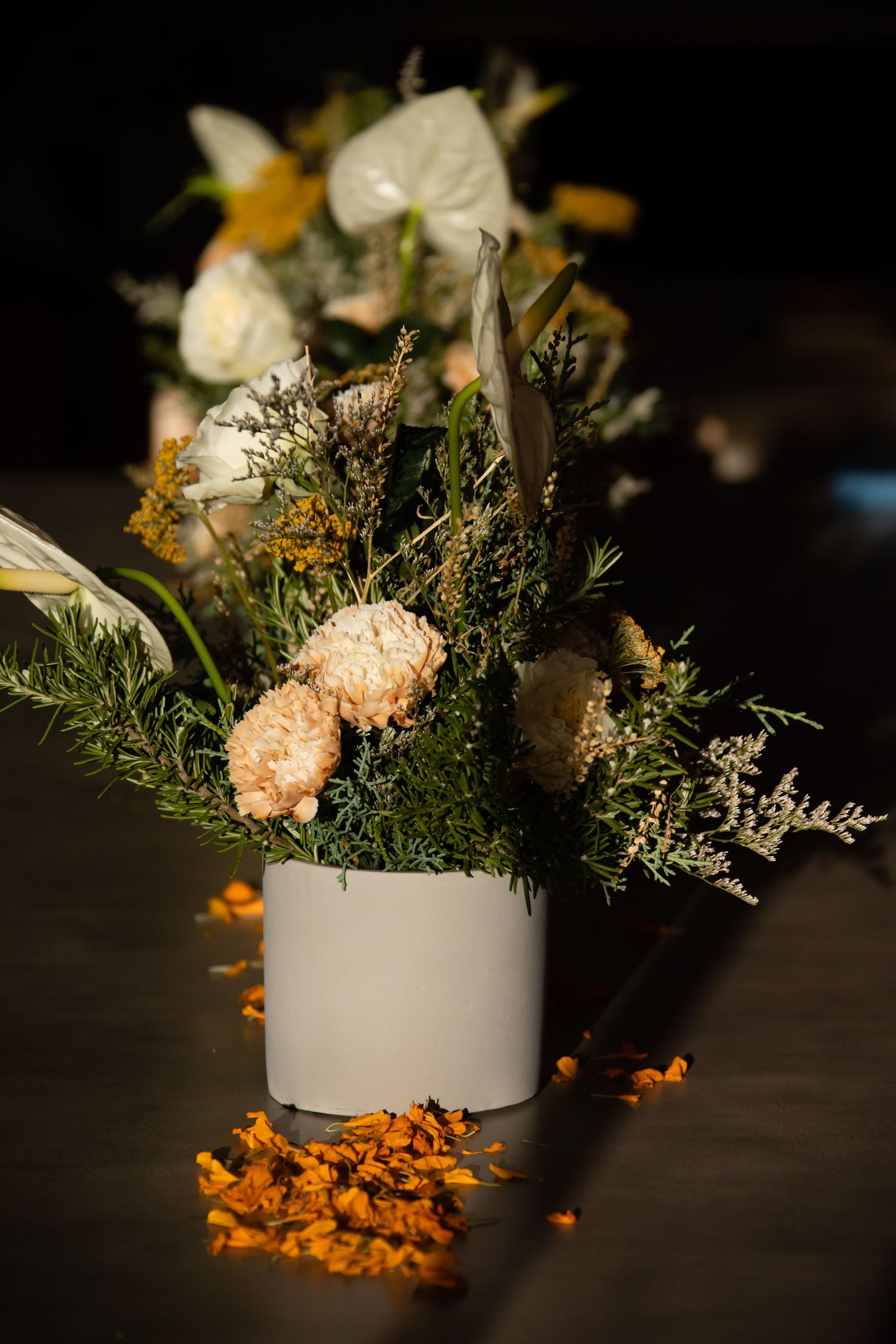 Floral centerpiece with white and peach flowers in a white vase against a dark background.