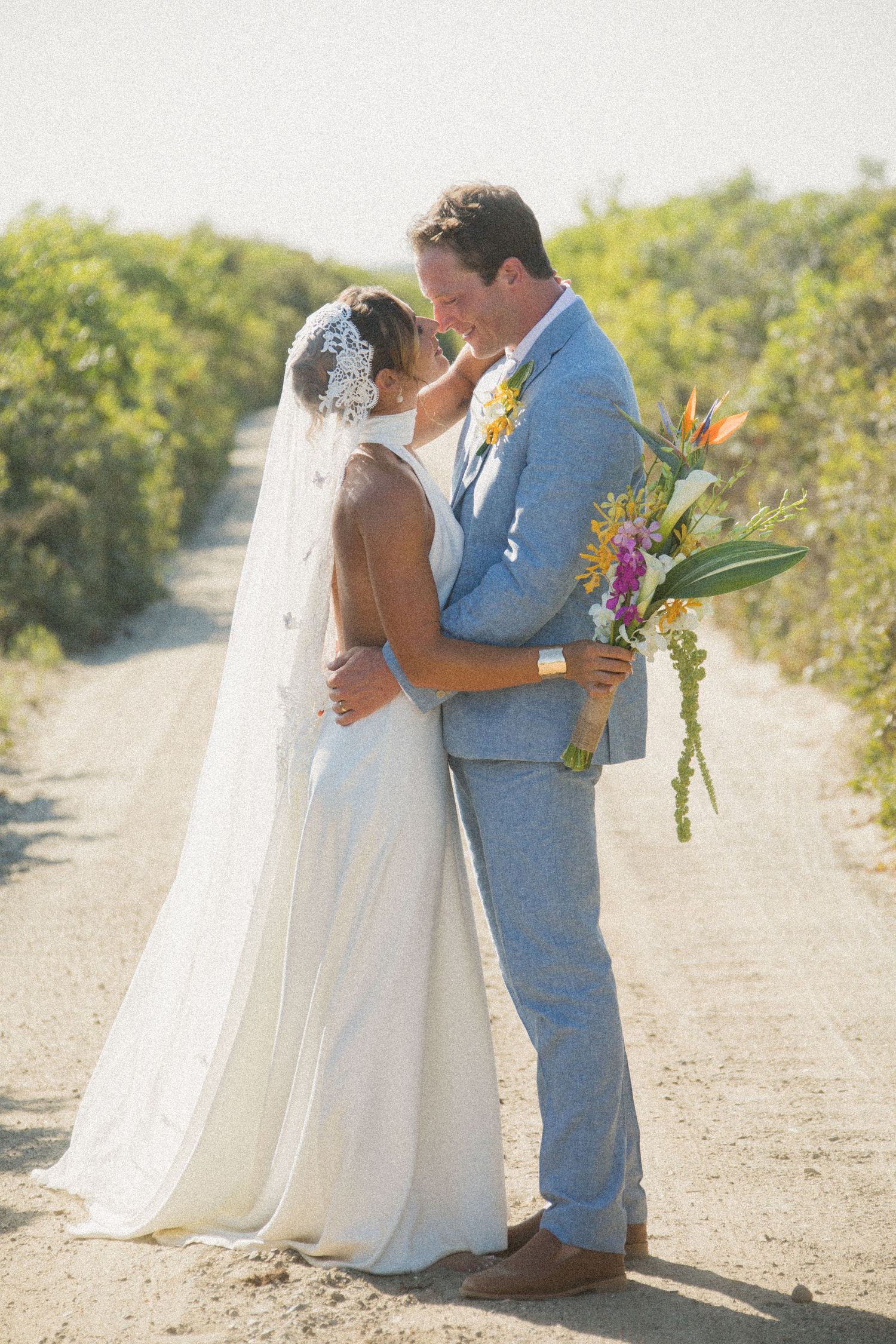 Wedding couple shares candid moments on a scenic dirt path with lush greenery.
