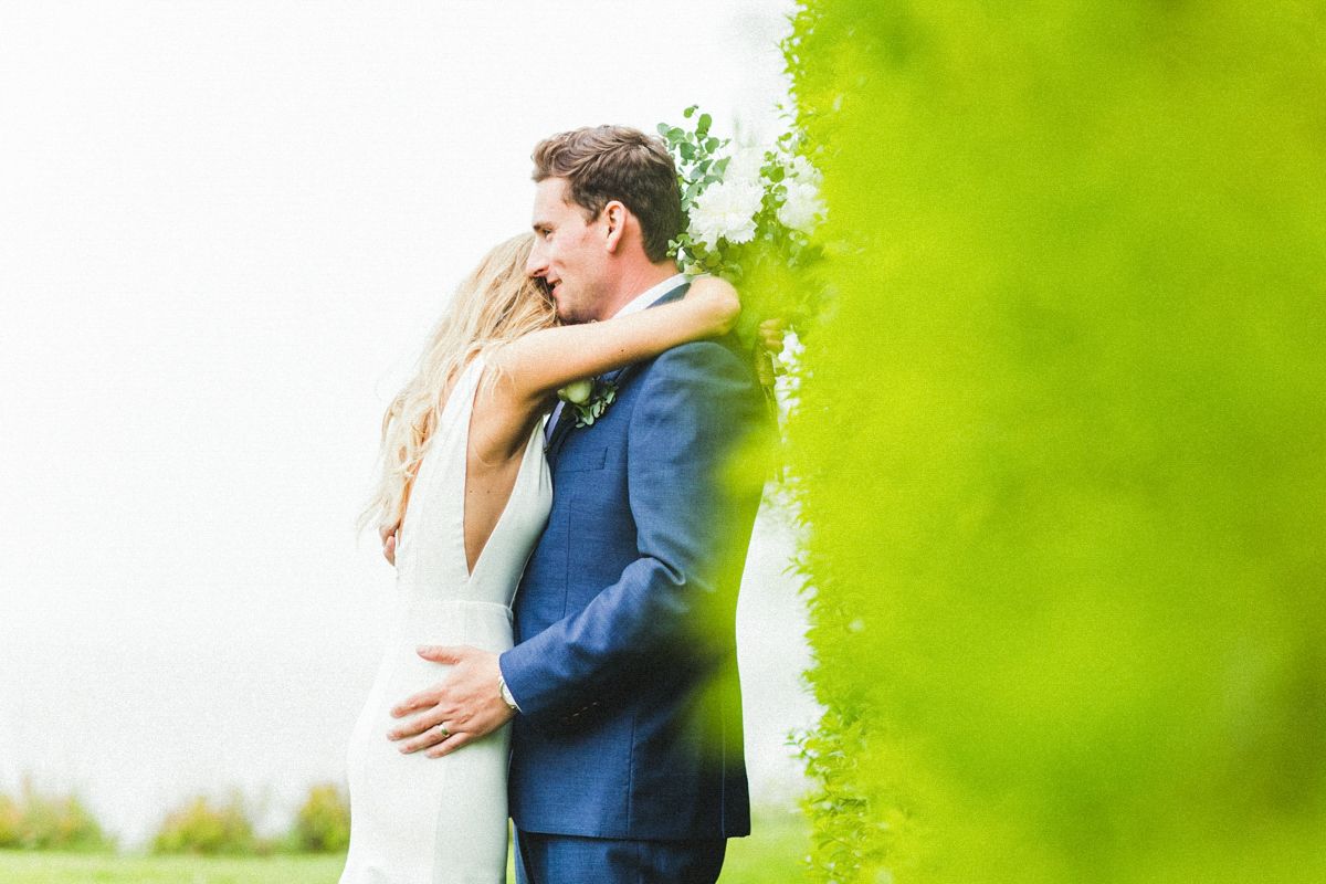A romantic embrace between newlyweds against a soft green background during their wedding photoshoot.