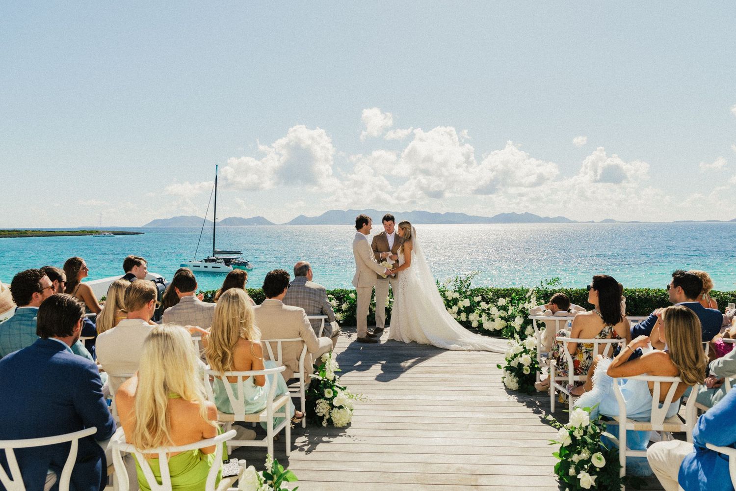 Guests seated at an outdoor beach wedding ceremony with ocean views and mountains in the background.