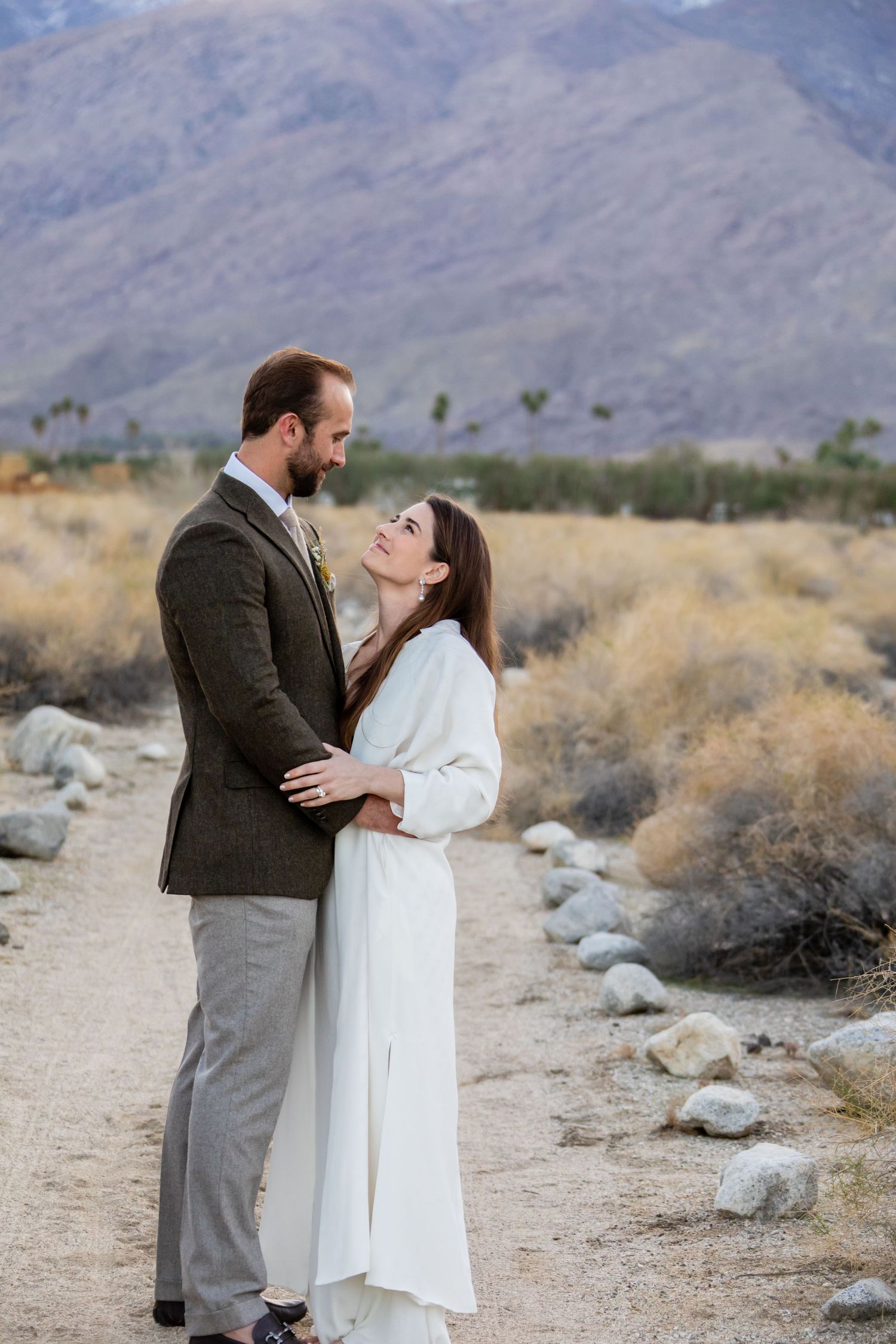 A romantic moment between a couple in formal attire against a desert mountain landscape.