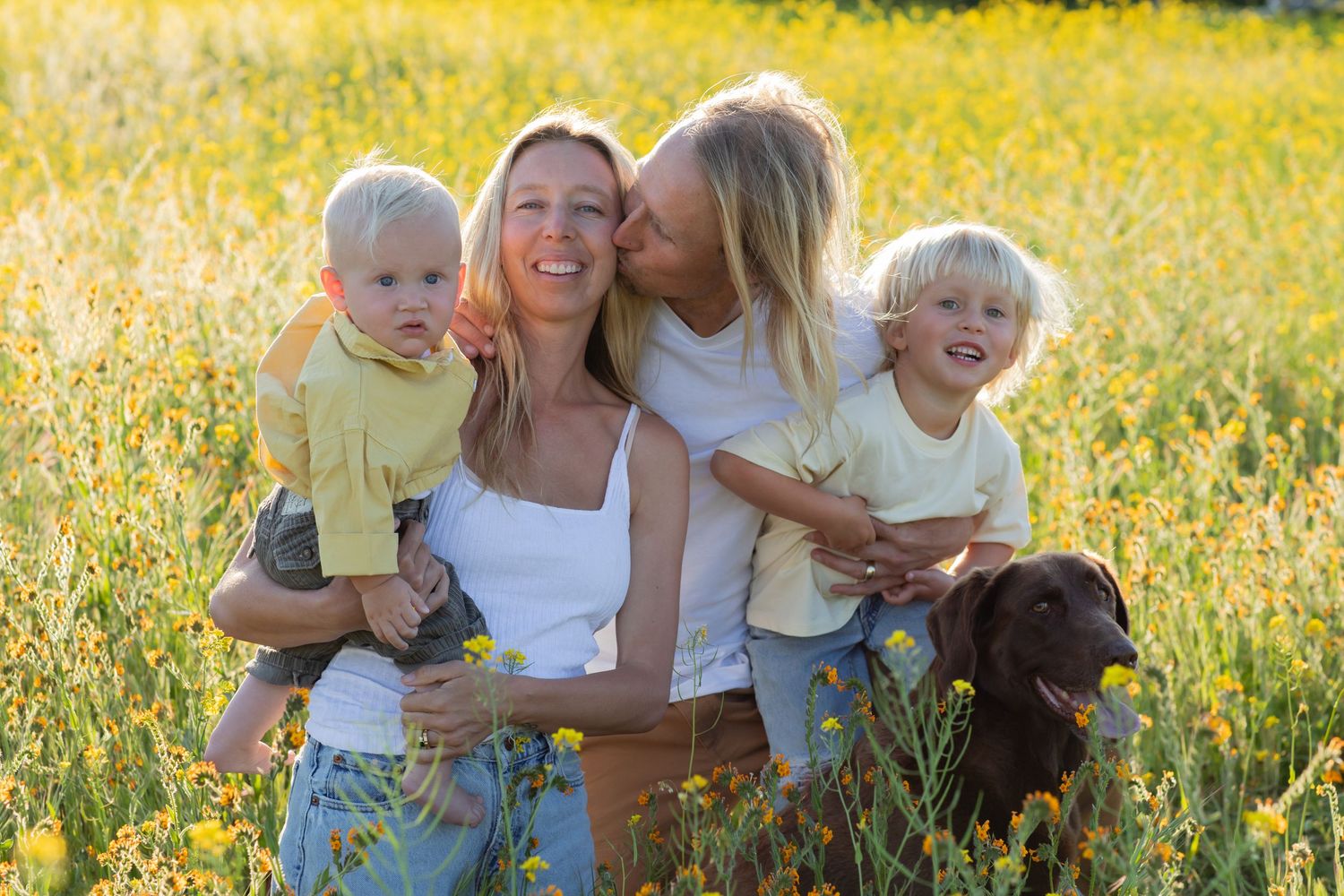 A group poses together in a field of yellow wildflowers with a dog.