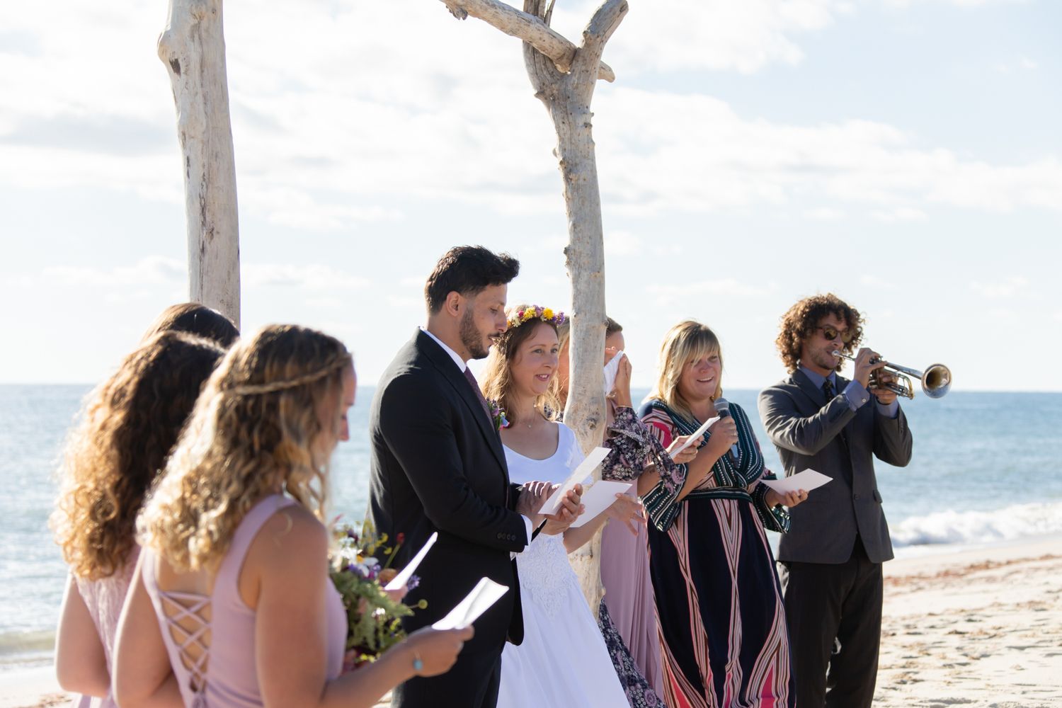 A wedding ceremony taking place on the beach with attendants holding programs.