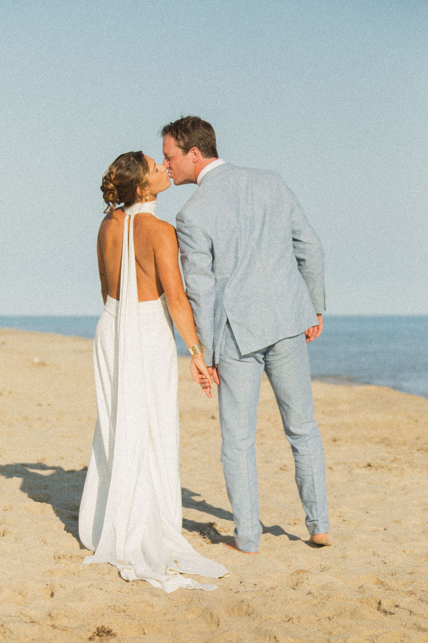 Intimate moment between newlyweds on sandy beach with ocean view.