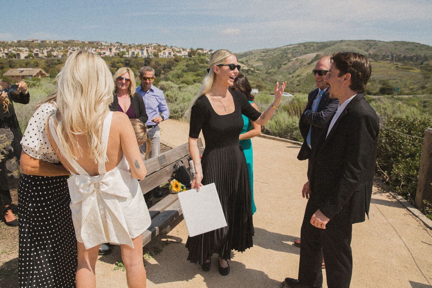 Wedding guests gathered on a scenic overlook with hills and ocean in the background.