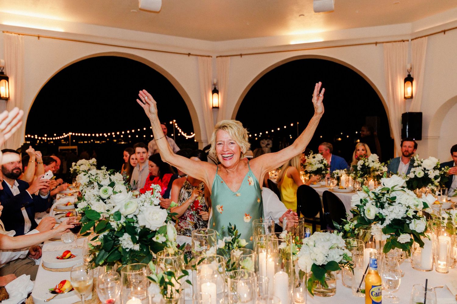 Festive wedding reception scene with decorated tables, string lights, and floral arrangements.