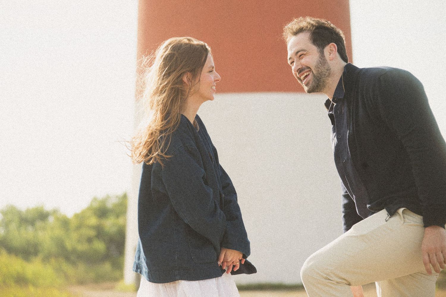 Couple sitting together against lighthouse wall during sunset photo session.