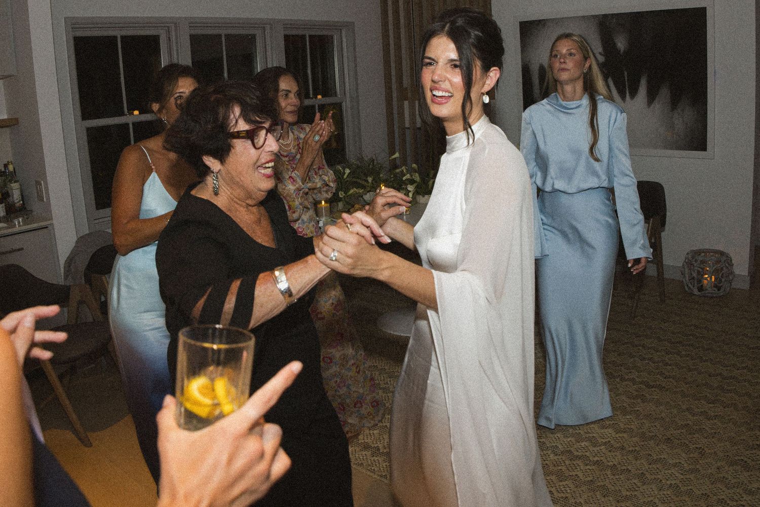 Bride in white gown dancing joyfully with a guest at an elegant indoor wedding reception.