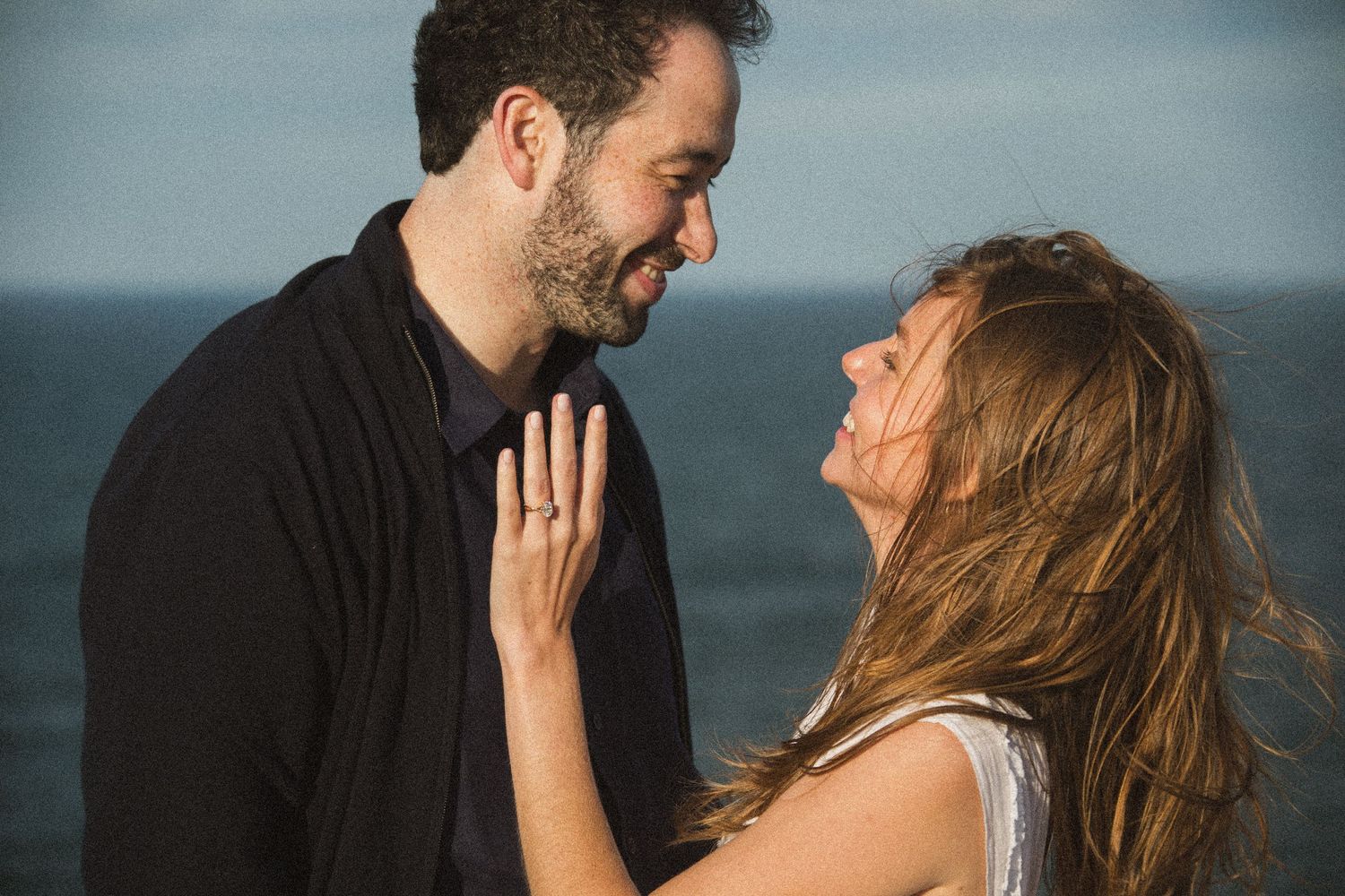 A romantic seaside photoshoot shows a couple embracing against an ocean backdrop.
