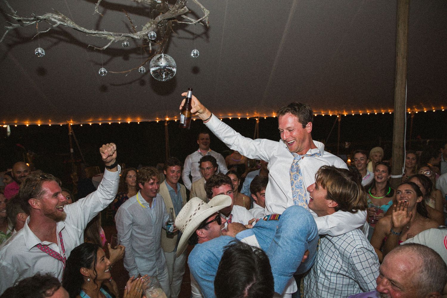 Lively wedding reception dance party with guests celebrating on a crowded dance floor under string lights.