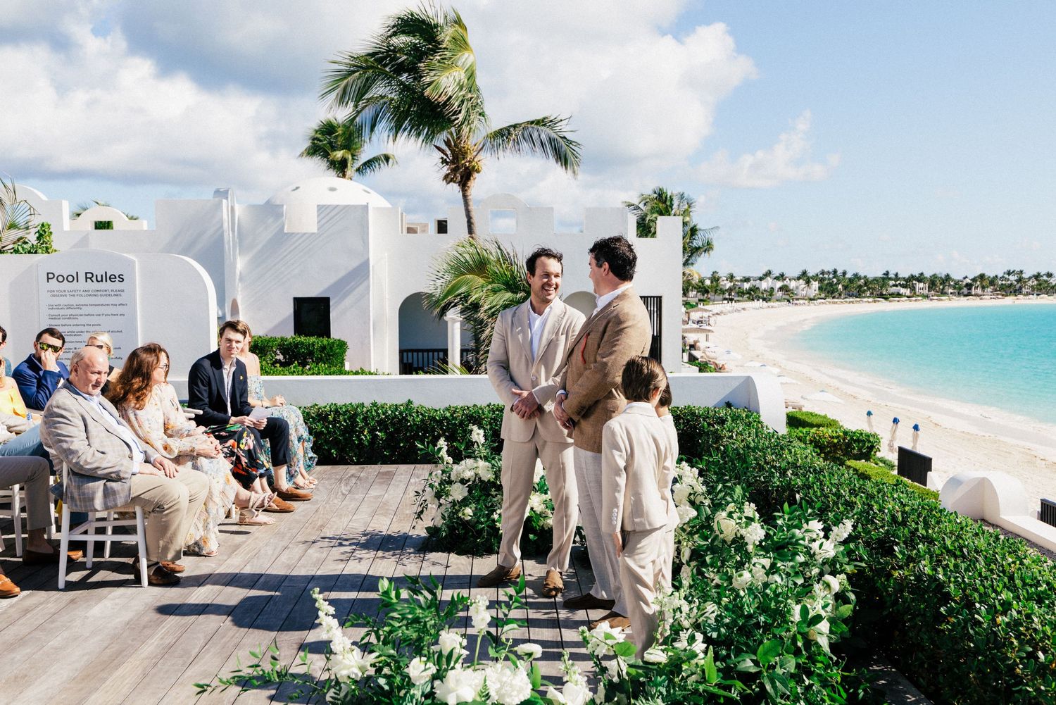 Beachfront wedding ceremony setup with white chairs and tropical landscaping overlooking turquoise waters.