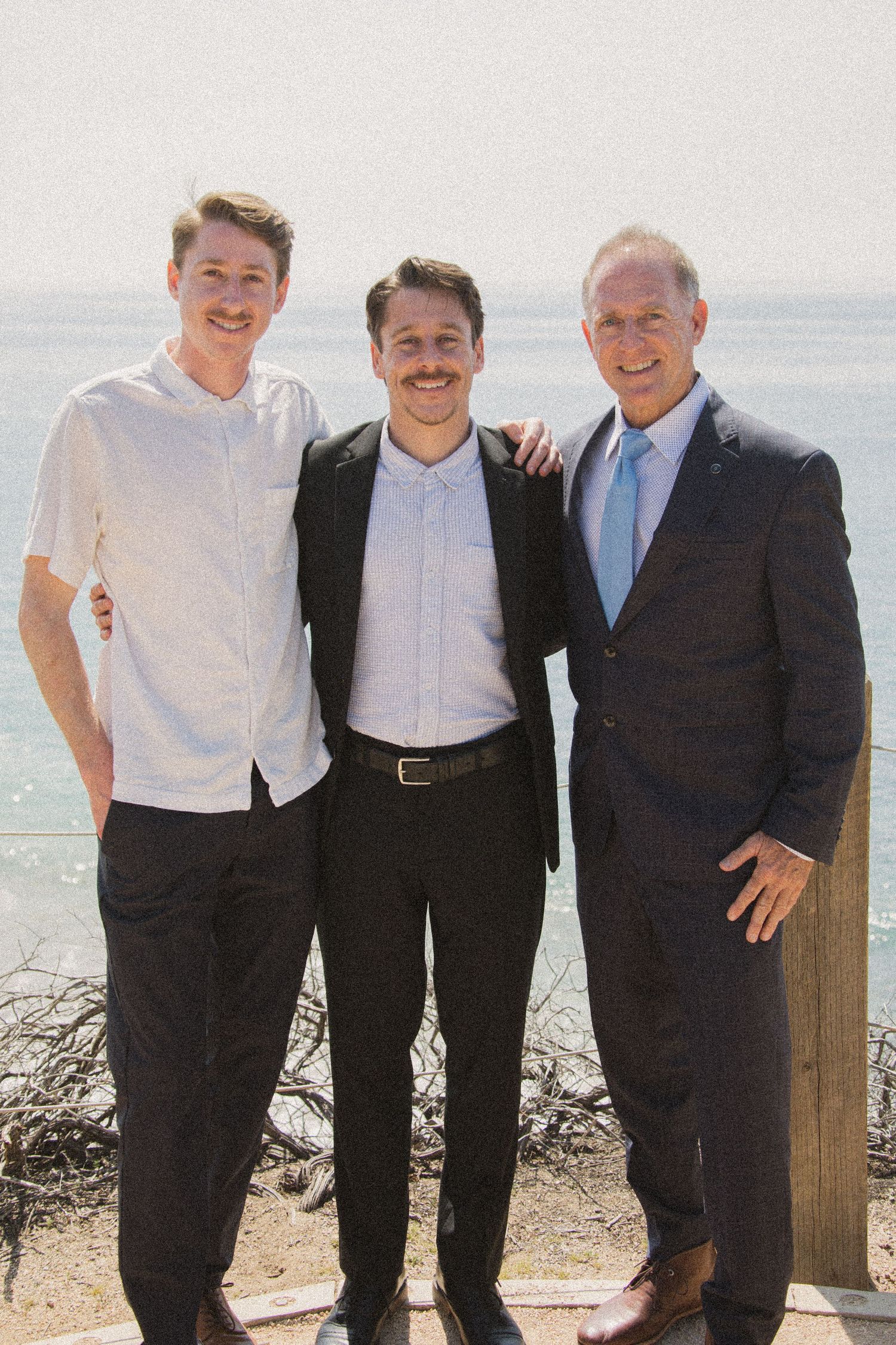 Group photo of men in formal attire standing together at an oceanside location.