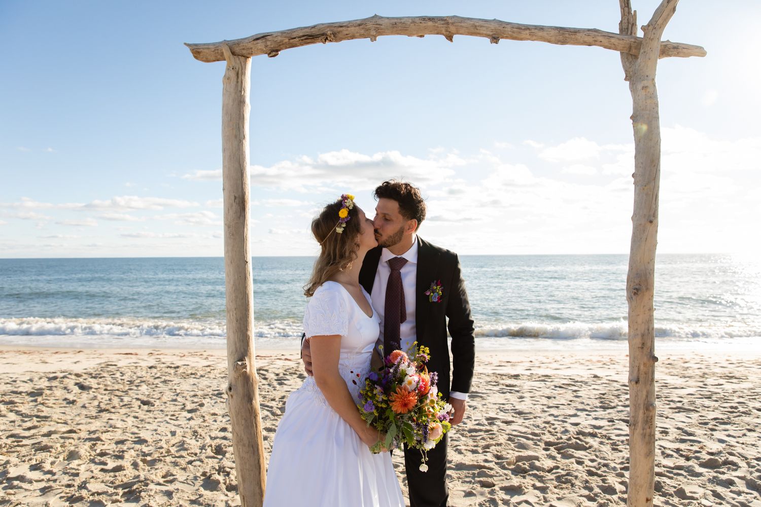Coastal wedding ceremony site with rustic wooden arch and sparkling ocean backdrop.