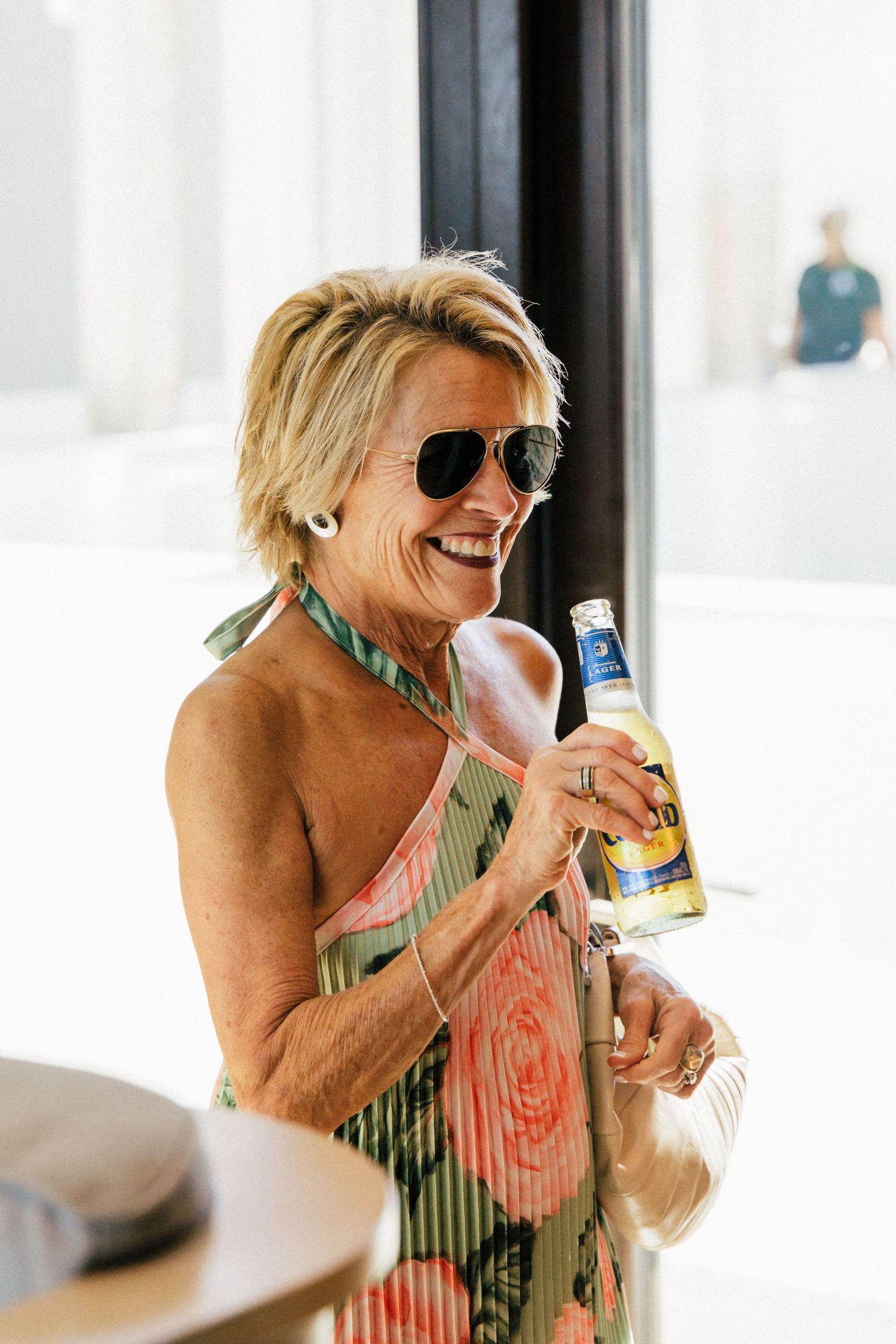 Guest in floral dress laughing while holding a beverage at wedding celebration.