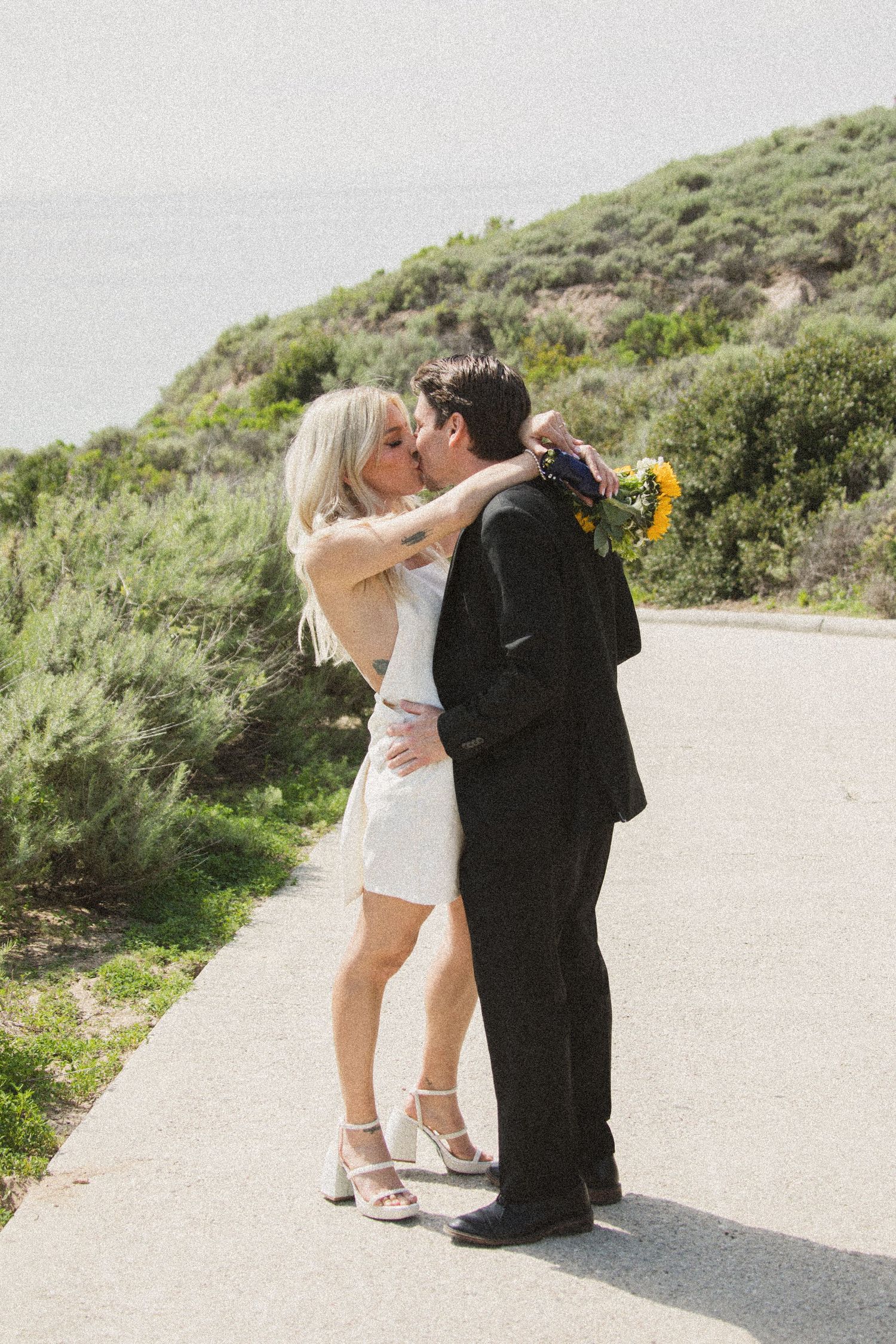 Newlyweds sharing intimate moments on scenic outdoor path surrounded by greenery.