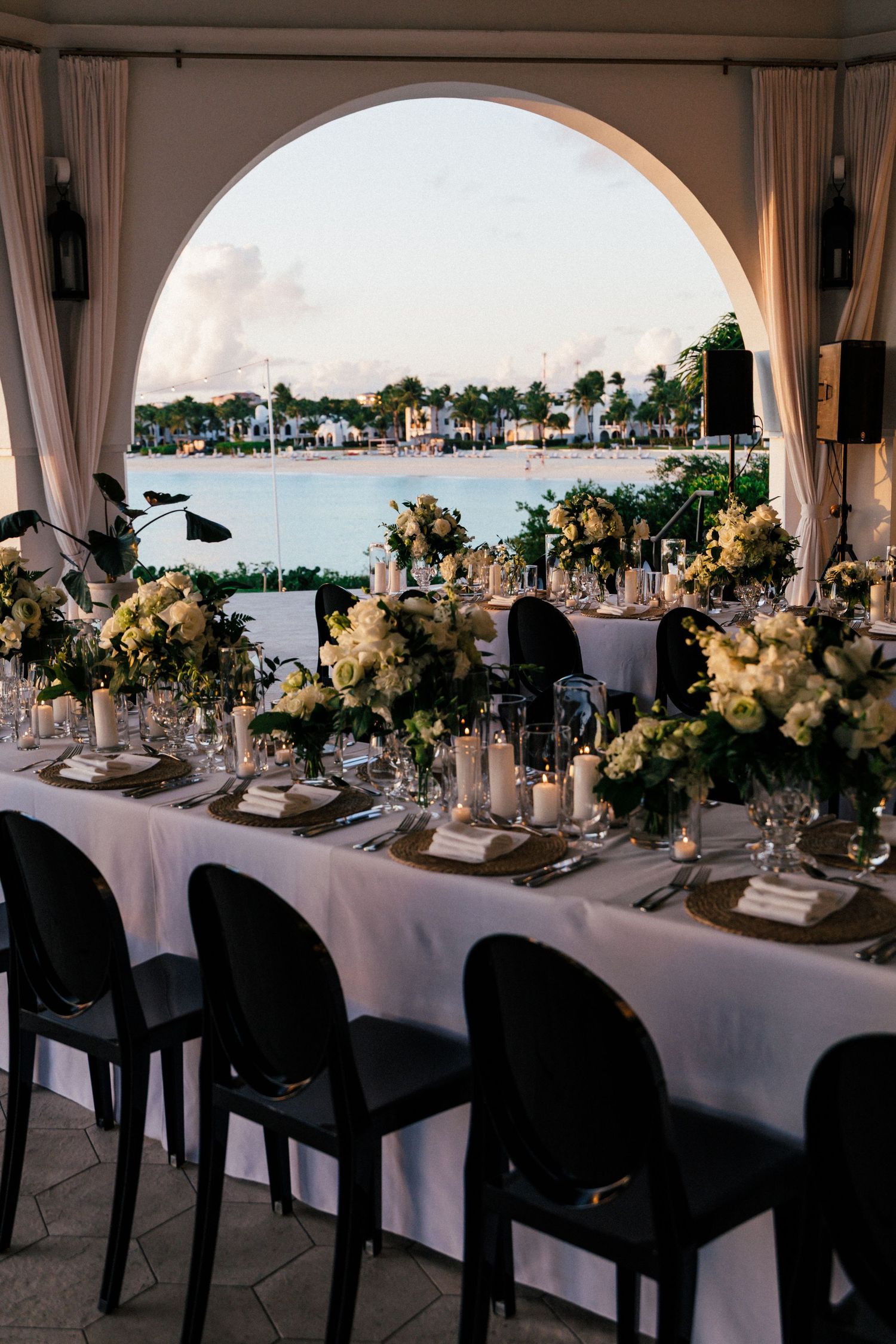 Elegant wedding table setting framed by arched window overlooking waterfront view.