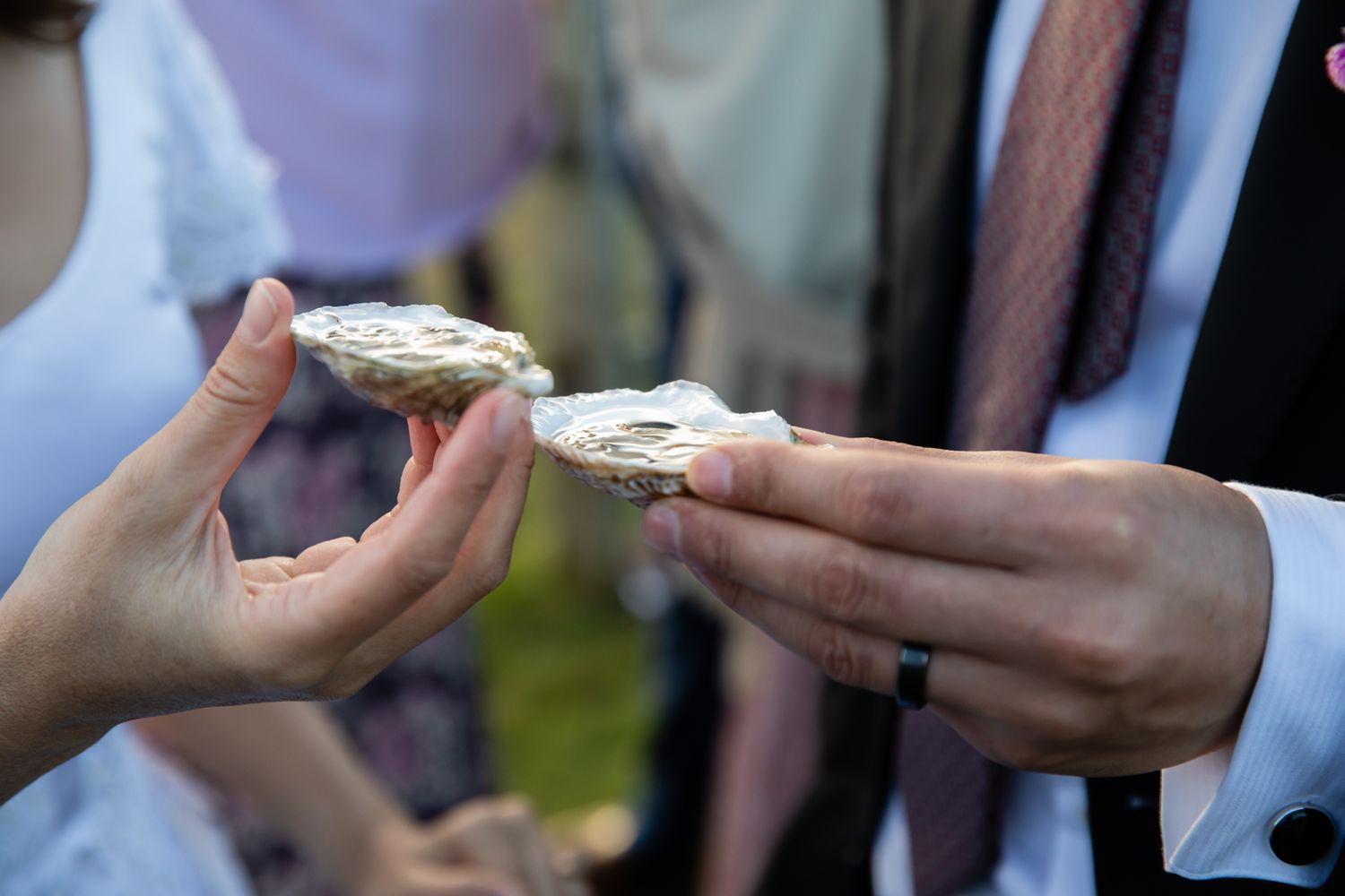 Hands holding fresh oysters during an outdoor celebration.