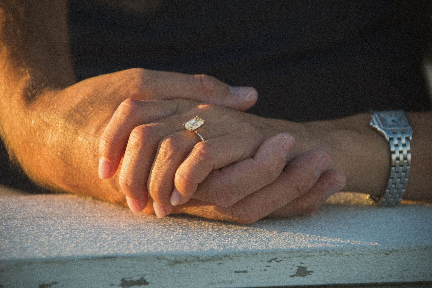 Close up details of hands resting together on a white surface.