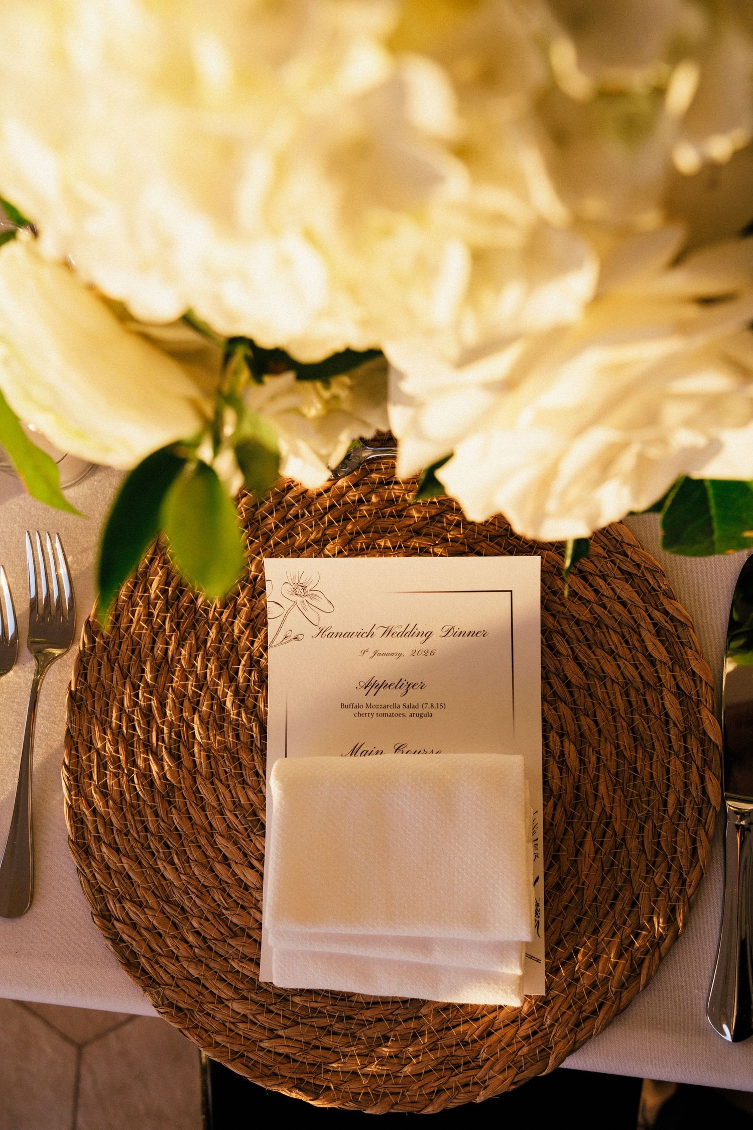 Wedding place setting with woven charger plate and menu card surrounded by white flowers.