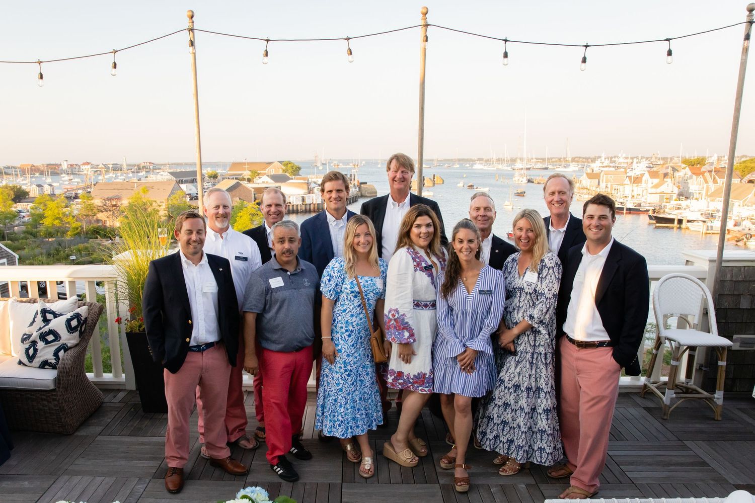 Group of professionals posing on a rooftop deck with a scenic harbor view at sunset.