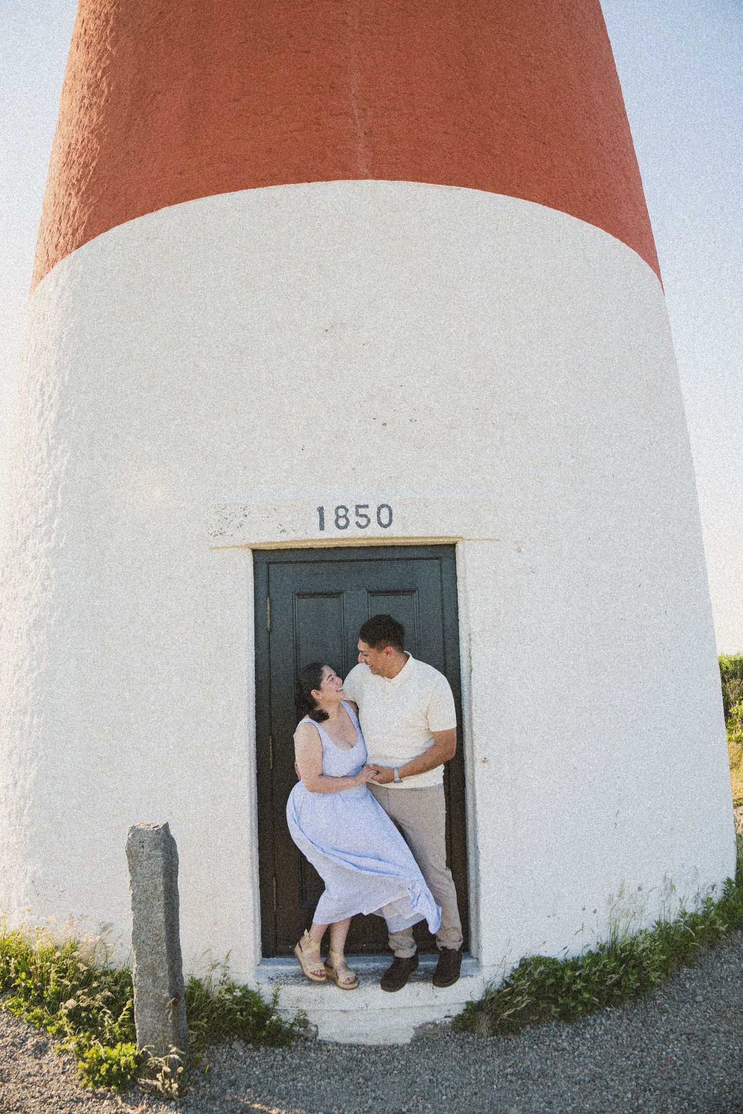 Couple embracing in doorway of historic 1850 lighthouse with red and white exterior.