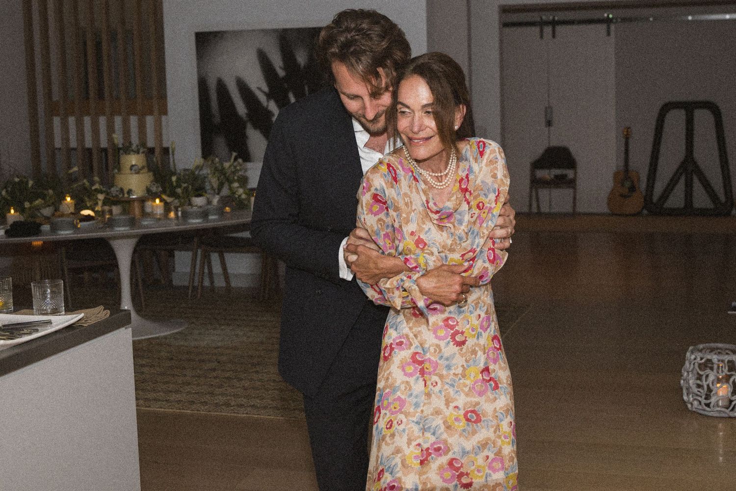 Couple sharing a warm embrace in a softly lit modern interior space, woman wearing a floral dress.