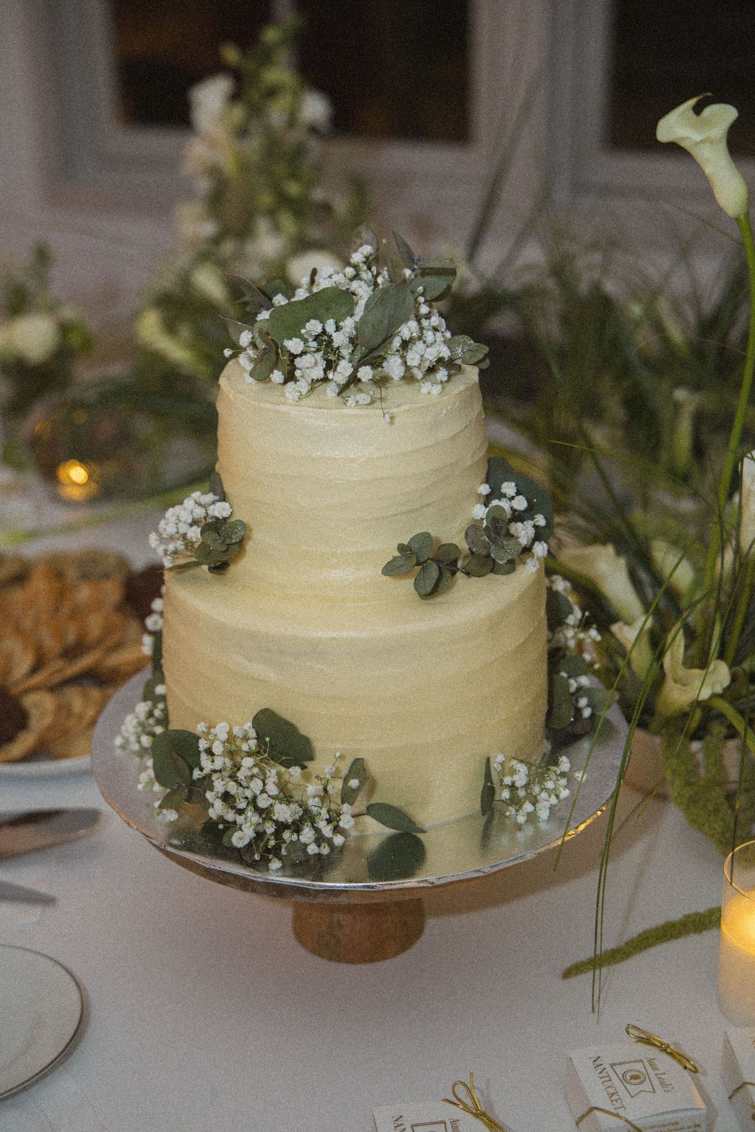 Two-tier white wedding cake with baby's breath and eucalyptus on a wooden cake stand.