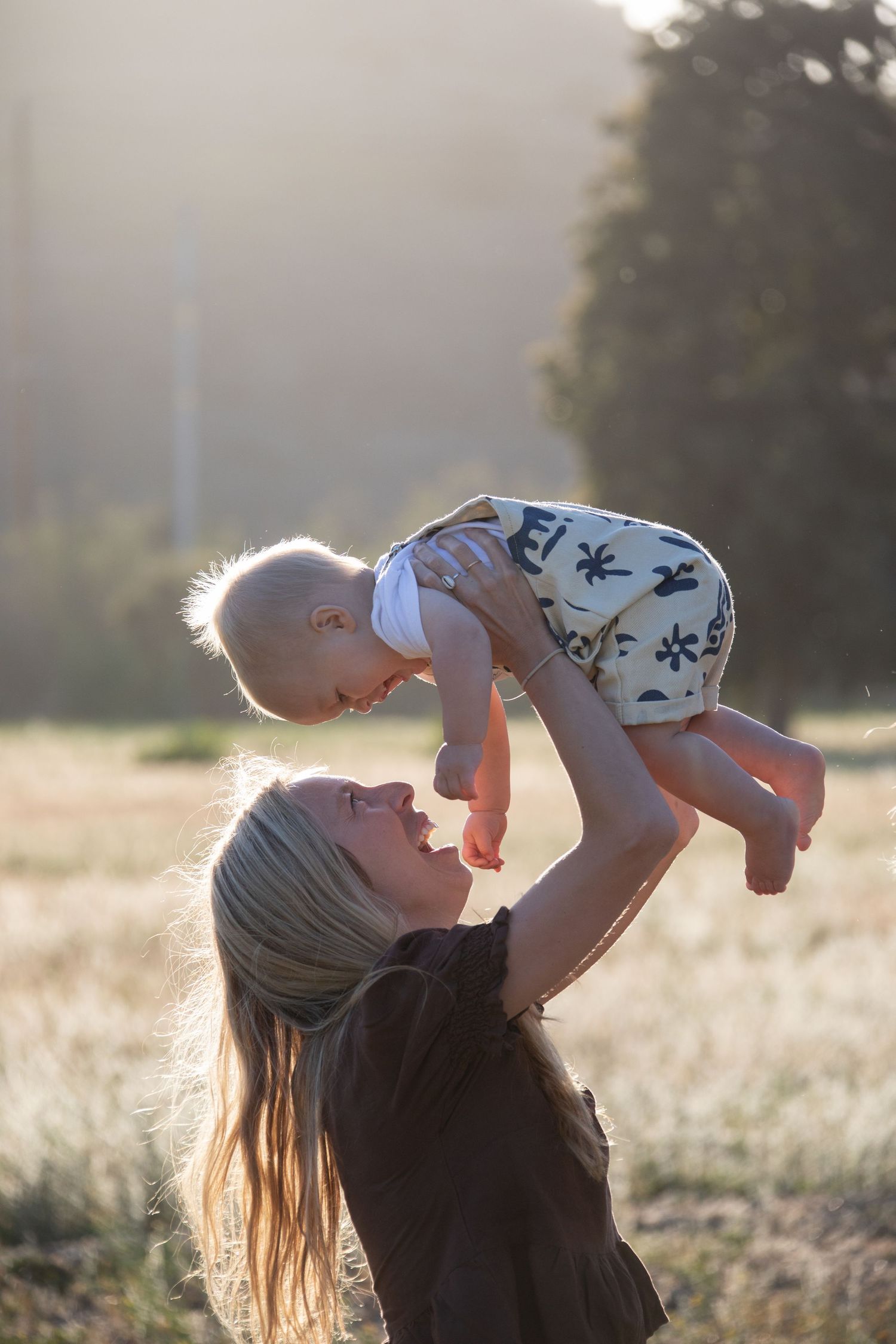 A parent lifts a baby high in the air during a sunset photoshoot.