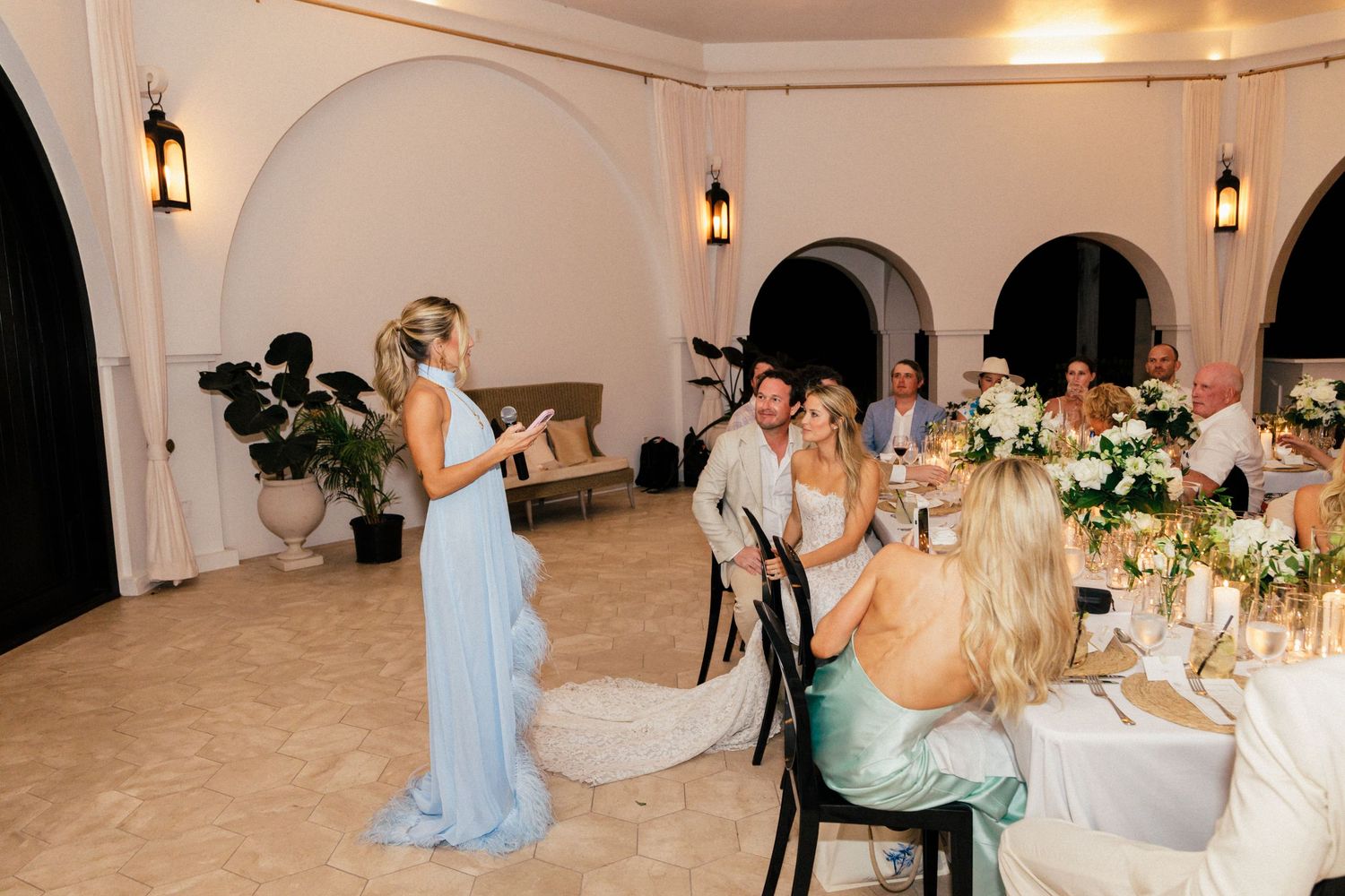 Wedding reception dinner setup with elegant table settings and hanging lanterns in a white-walled venue.