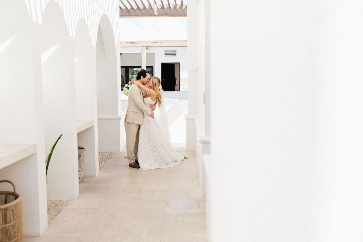 A romantic wedding moment captured in a white archway corridor with Mediterranean architectural details.