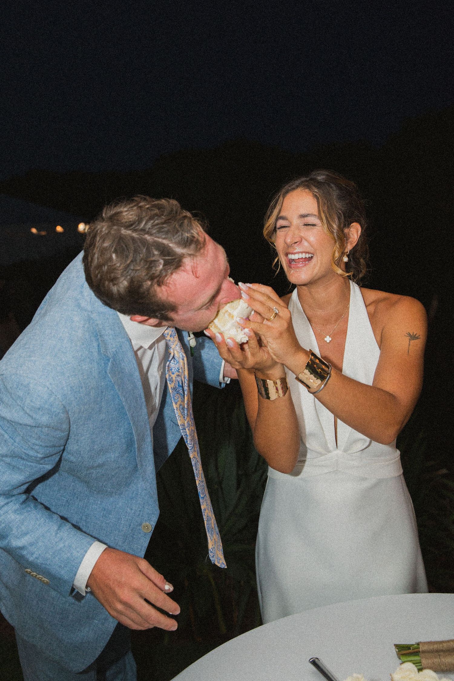 Playful moment between newlyweds during cake cutting at outdoor evening reception.