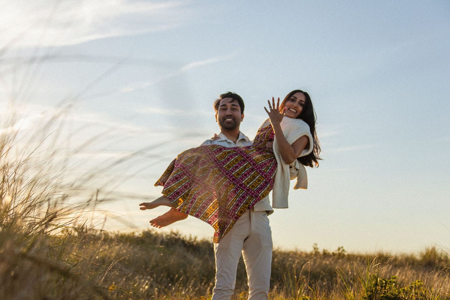 Couple playing and laughing together in a grassy field at sunset.
