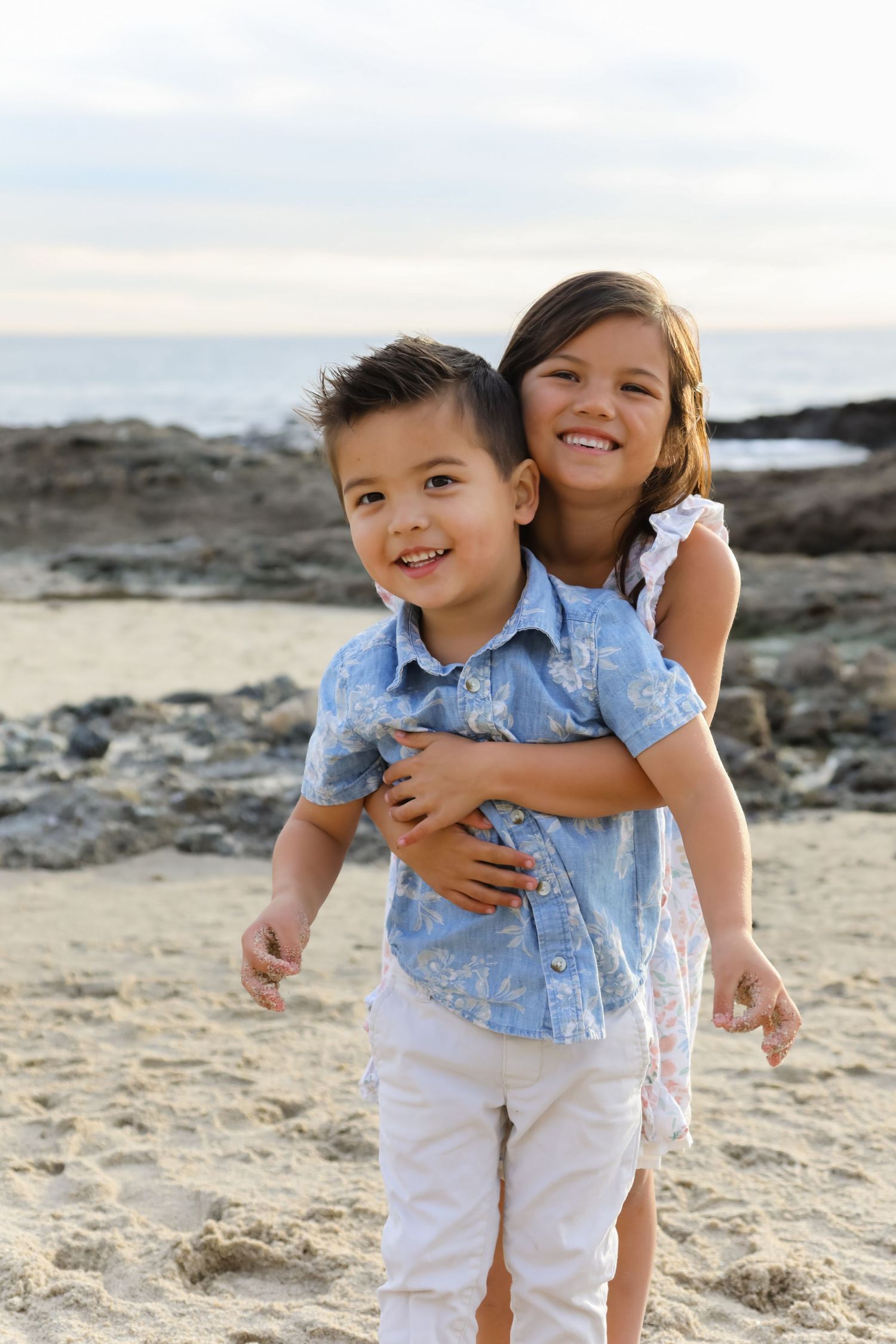 Two children embrace while playing and laughing together on a sandy beach.