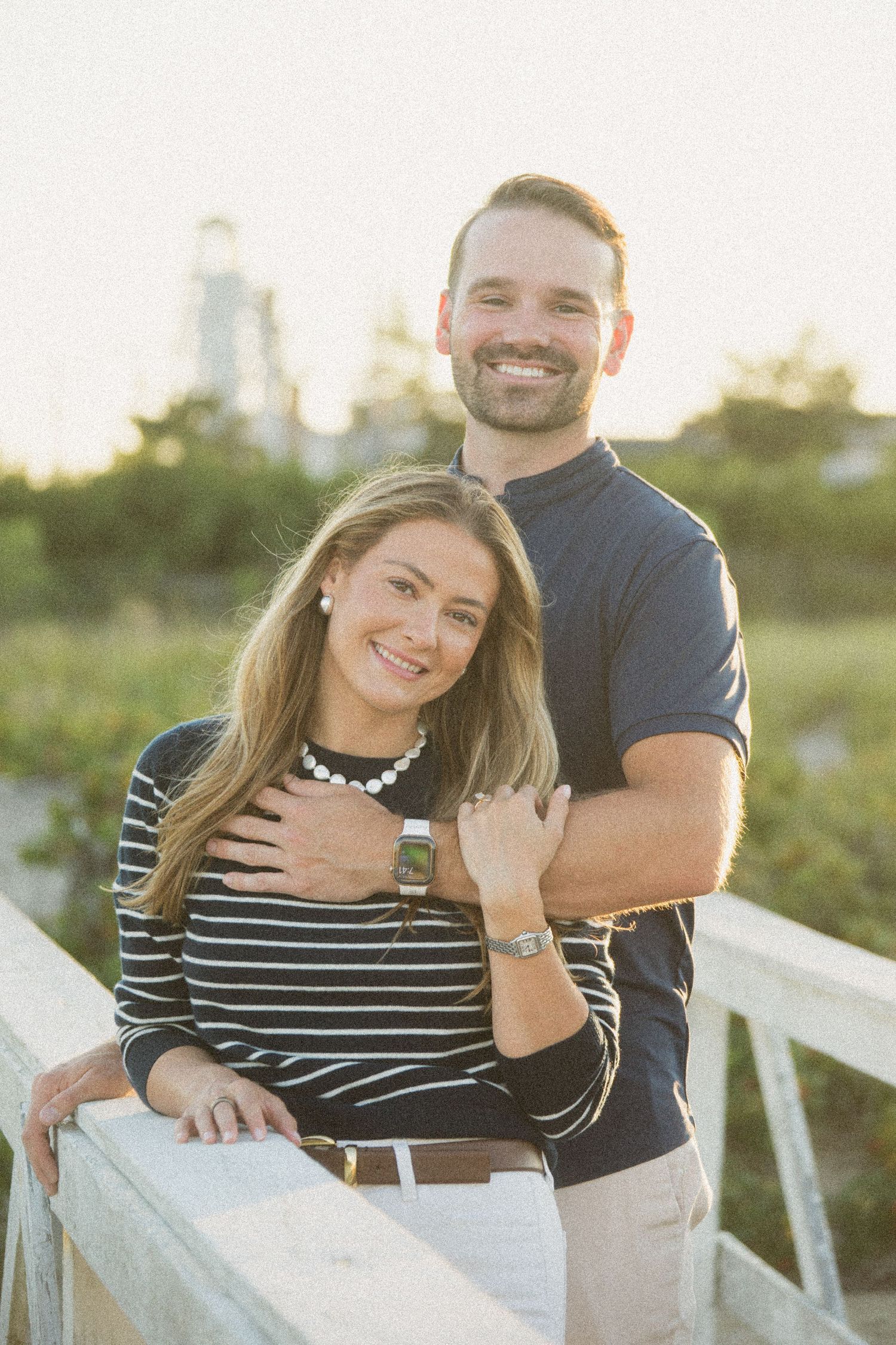 Happy couple sitting together on white bench during engagement photoshoot.