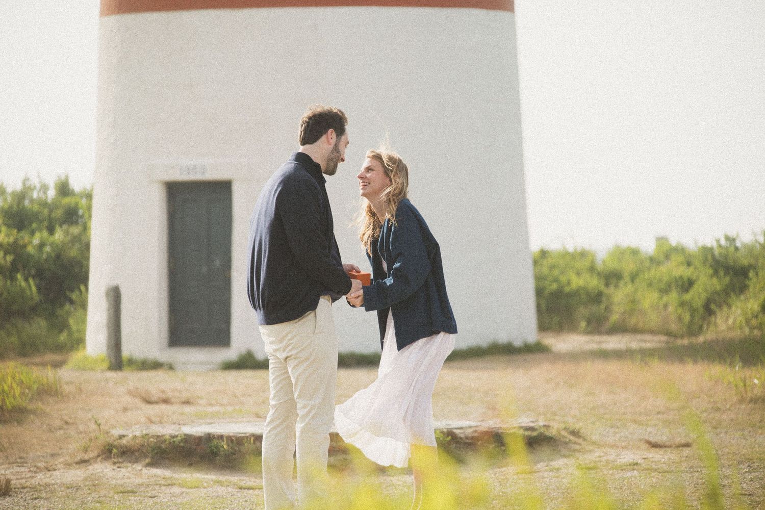 Romantic moment captured at base of white lighthouse on coastal path.