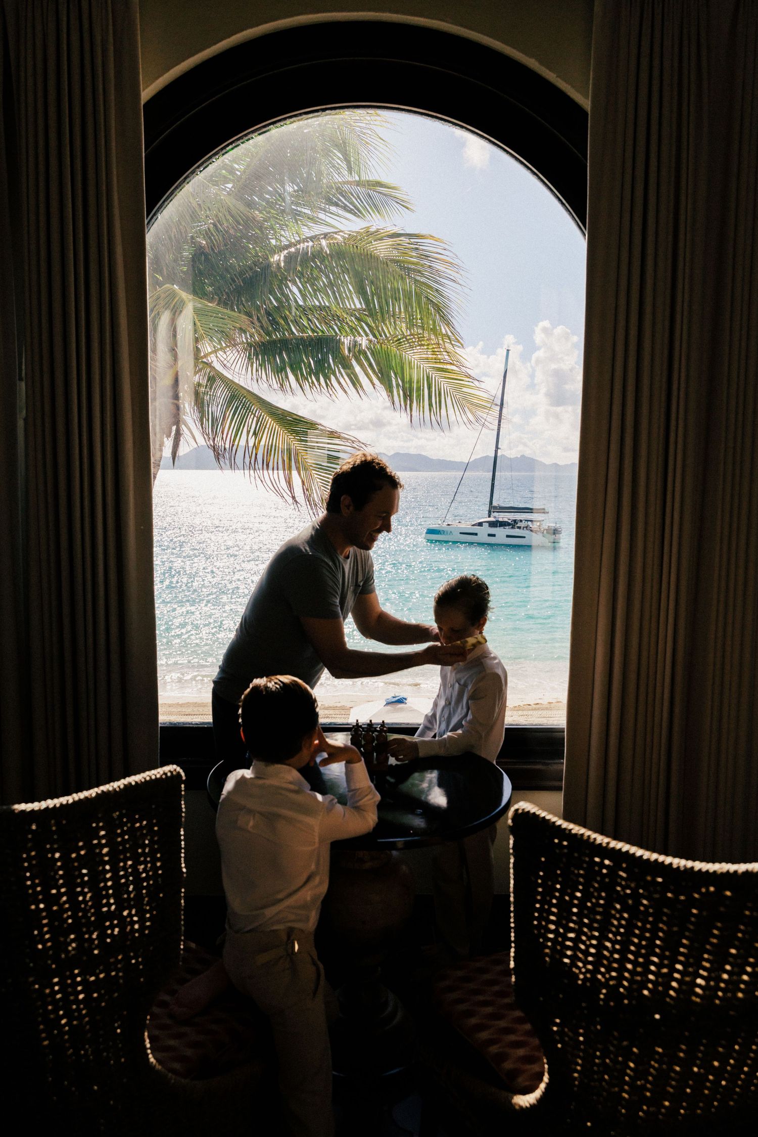 Silhouetted figures in arched window frame with ocean and sailboat view.