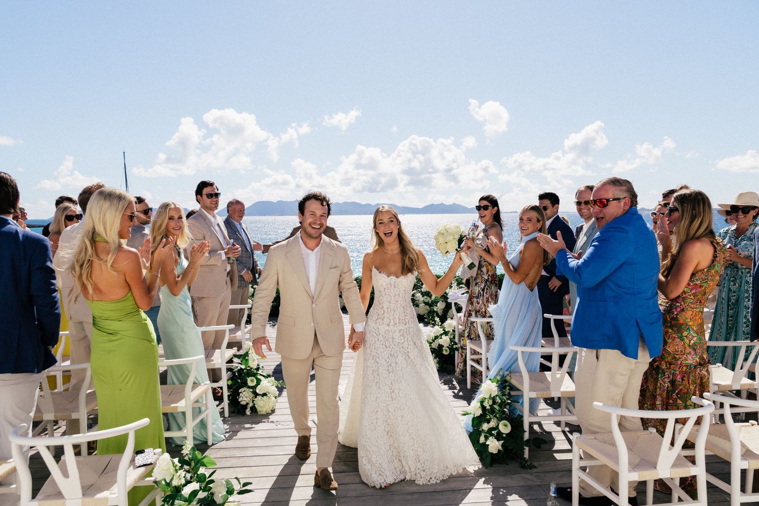 Elegant outdoor wedding ceremony setup with white chairs and floral arrangements against an ocean backdrop.