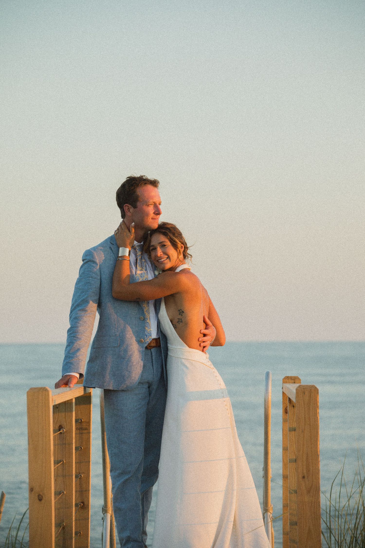 A couple leans against wooden posts overlooking the ocean during a sunset photoshoot.
