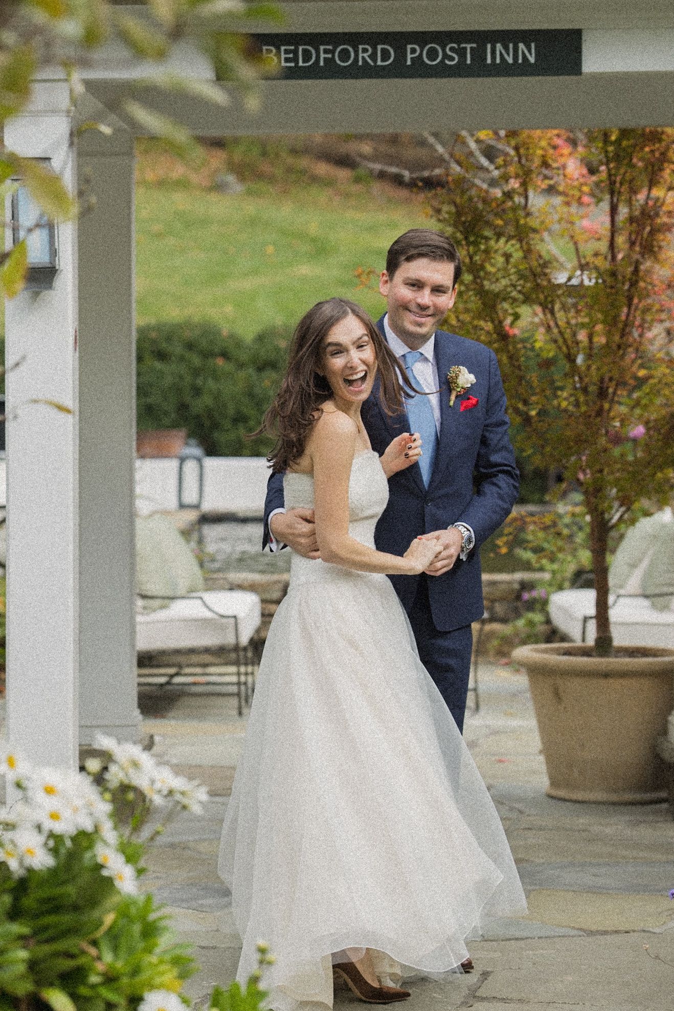 Laughing bride in a white tulle gown embraces her groom in a navy suit under a pergola at the Bedford Post Inn wedding.