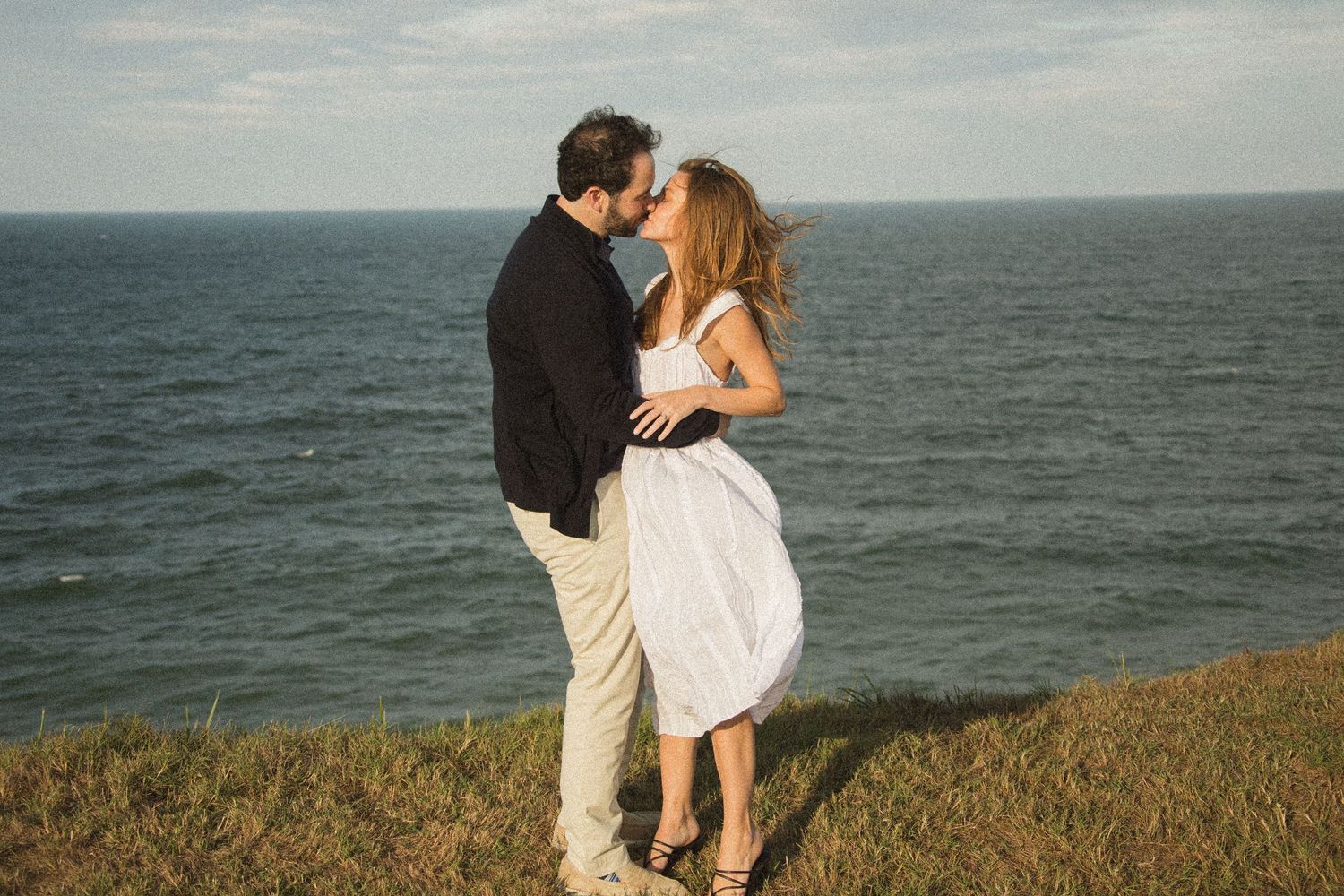 Two people share a romantic dance on an oceanside cliff during golden hour.