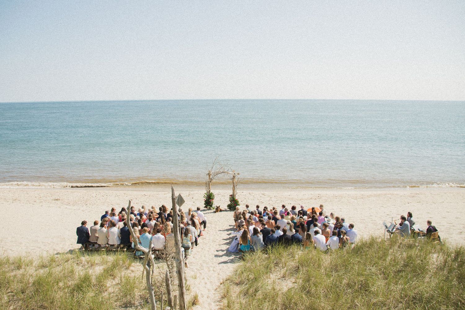 Wedding ceremony guests gathered on a beach with ocean views.