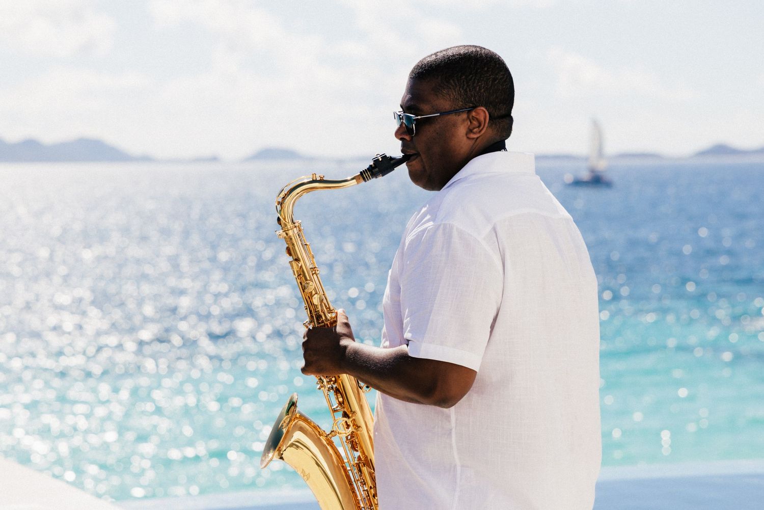 Musician in white playing saxophone against ocean backdrop.