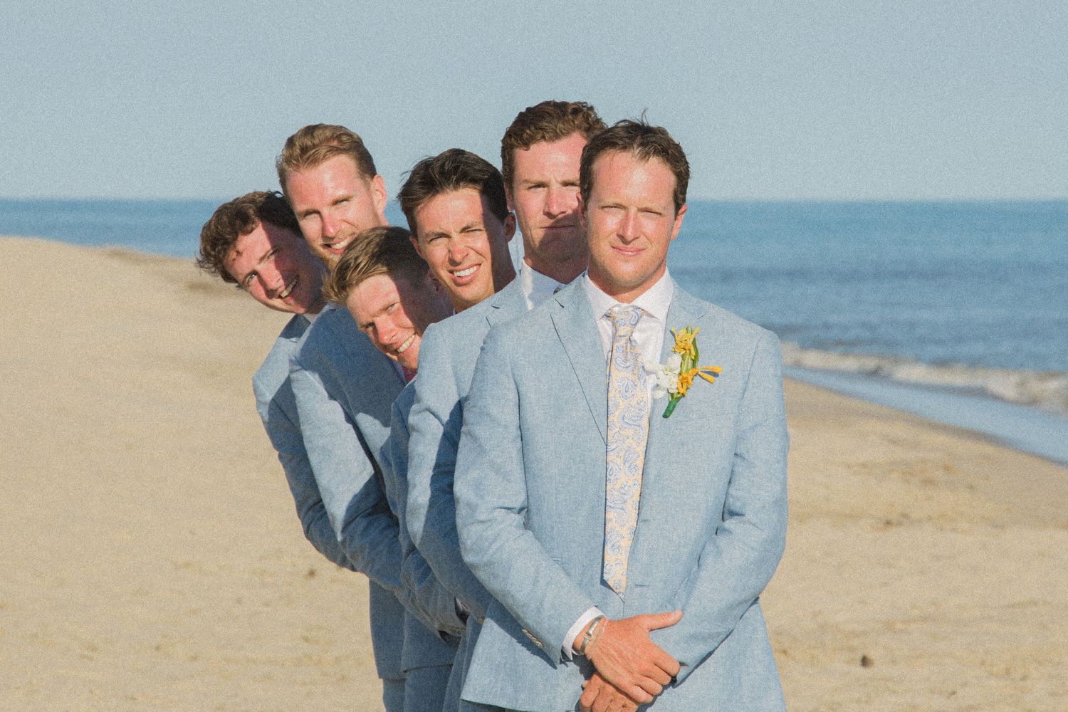 Groomsmen in light blue suits lined up on beach for wedding photo.