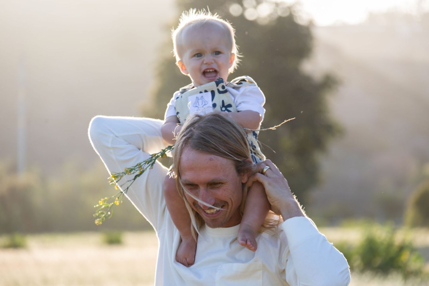 Family plays together in a sun-drenched field during golden hour photo session.