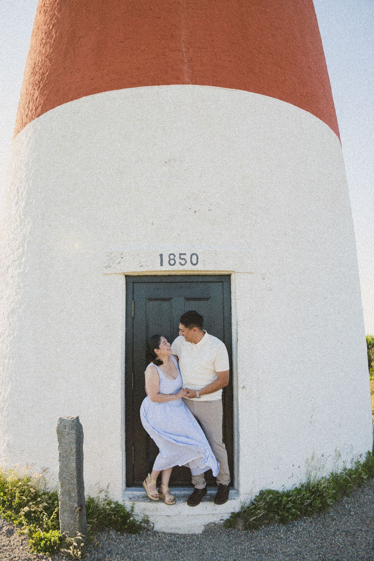 Couple embracing in doorway of historic 1850 lighthouse with red and white exterior.