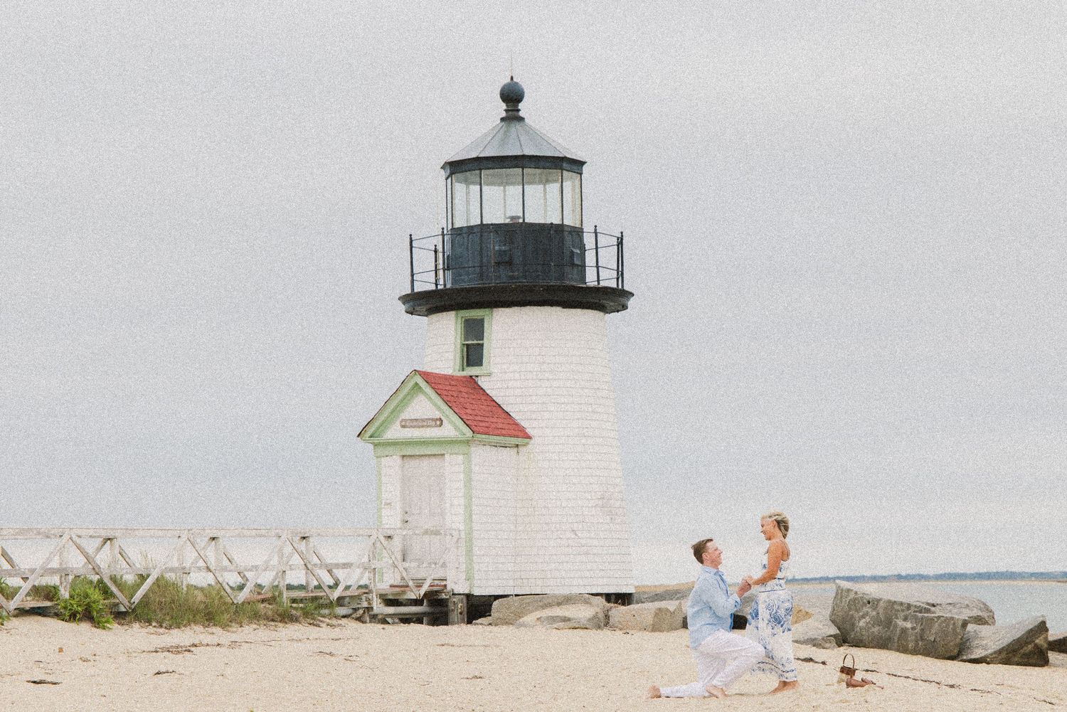 Couple dancing on sandy beach near Brant Point Lighthouse in Nantucket on a cloudy day.