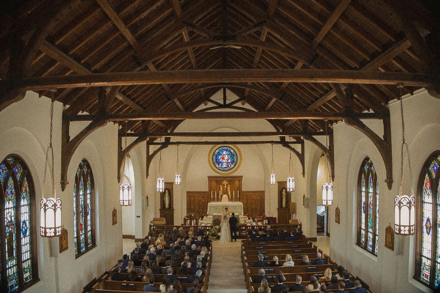 Guests fill the wooden pews of a historic church with exposed timber beams and stained glass windows during a wedding ceremony.